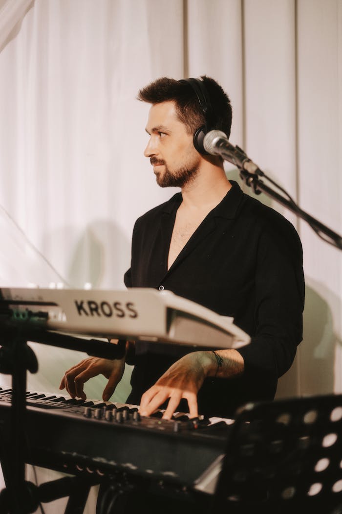 A male musician passionately playing a keyboard with a microphone setup on stage.